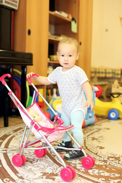 Vauva leikkii nukke ja rattaat — kuvapankkivalokuva