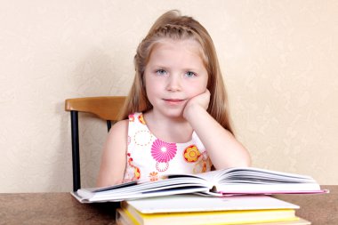 Little girl reading book in the kitchen against yellow wall at h clipart