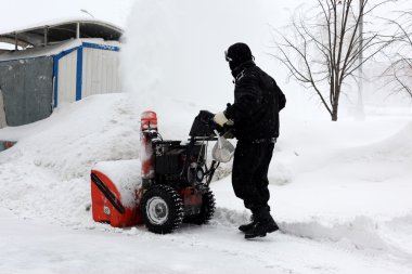 Snowblower in city under snowfall clipart