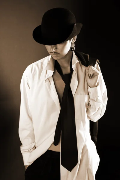 Young fashion model in hat, big man shirt and coat against black — Stock Photo, Image