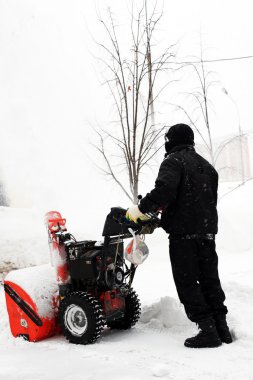 Snowblower in city under snowfall clipart