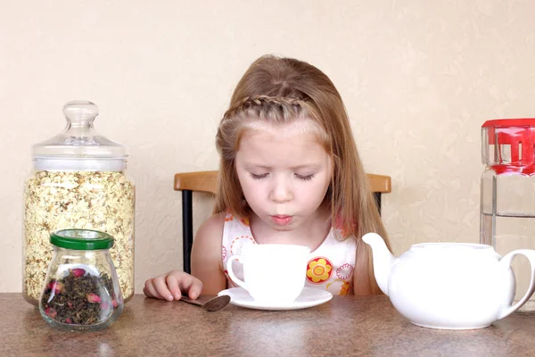 Маленькая девочка дует в чашку горячего напитка, за столом с лаймом, т — стоковое фото