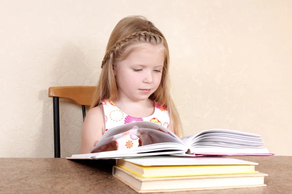 Little girl reading book in the kitchen against yellow wall at h — Stock Photo, Image