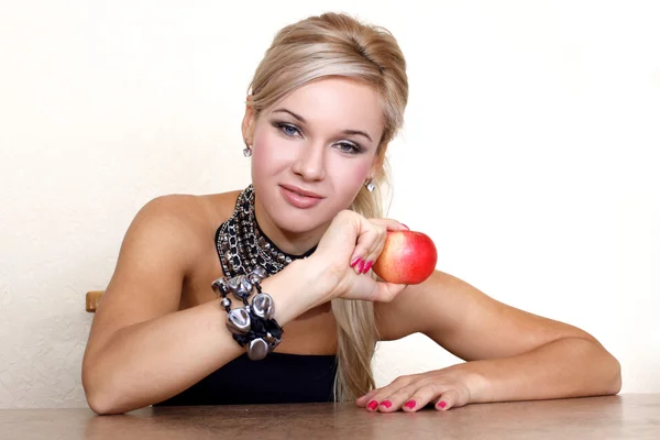 Жінка з червоним яблуком на жовтій стіні за столом — стокове фото
