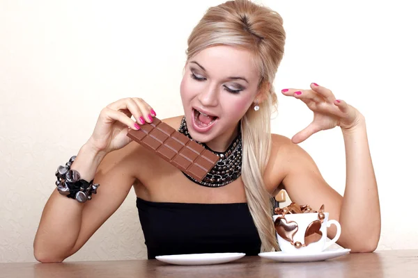 Woman with cup and chocolate against yellow wall at table — Stock Photo, Image