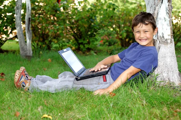 Jongen met laptop zitten op boom buitenshuis — Stockfoto