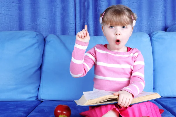 Überraschte kleines Mädchen mit Apfel und Büchern im Sofa — Stockfoto