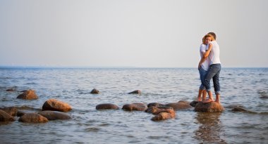 Couple embrace on a stone in sea clipart