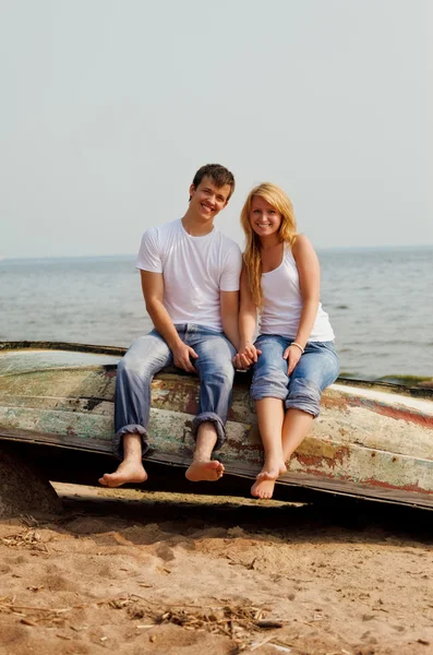 Casal em uma praia sentado no velho barco — Fotografia de Stock
