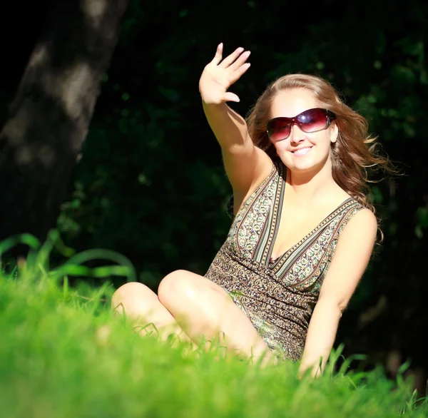 Dívka v sluneční brýle sedí v trávě — Stock fotografie