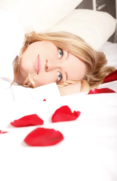 金发女人躺在床上用红色的玫瑰花瓣 — 图库照片