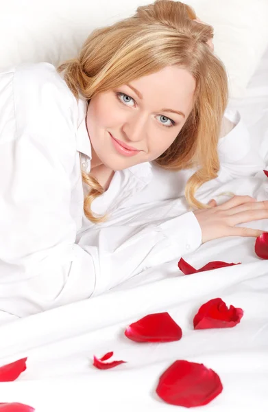 Glückliche Frau im Bett mit Rosenblättern — Stockfoto