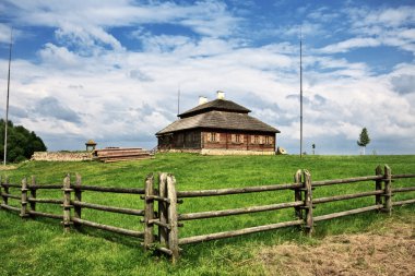 Wooden cottage on green hill under cloudy sky clipart