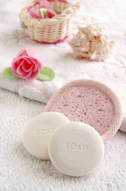 Two round soaps in a spa-saloon with soap roses and a pink sponge, vertical clipart