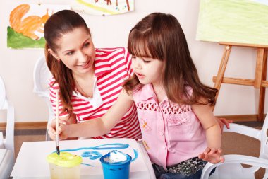 Child with teacher draw paints in play room. clipart