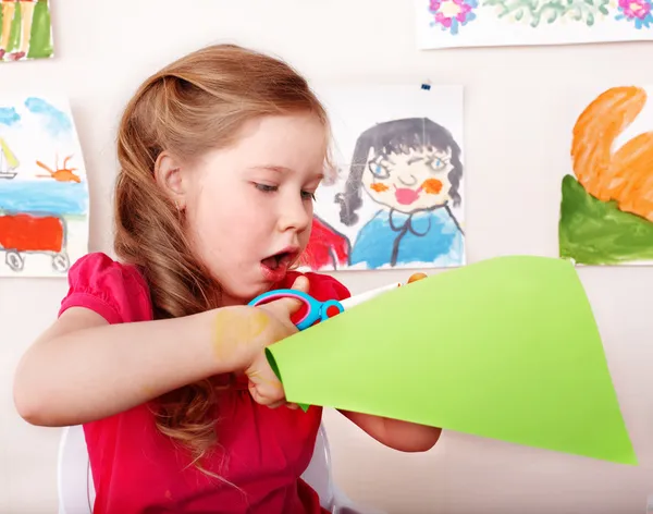 Ребенок с ножницами режет бумагу в игровой комнате . — стоковое фото