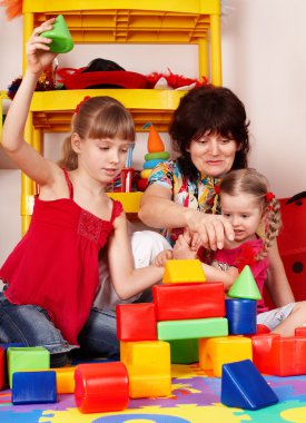 Children with block and senior woman in play room. clipart