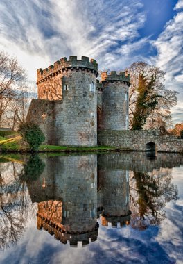 Ancient Whittington Castle in Shropshire, England reflecting in a calm moat round the stone buildings and processed in HDR clipart