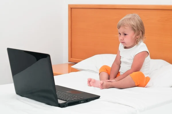 Una niña pequeña está sentada con un portátil en la cama — Foto de Stock