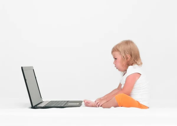 A small girl is sitting with a laptop on the bed — Stock Photo, Image