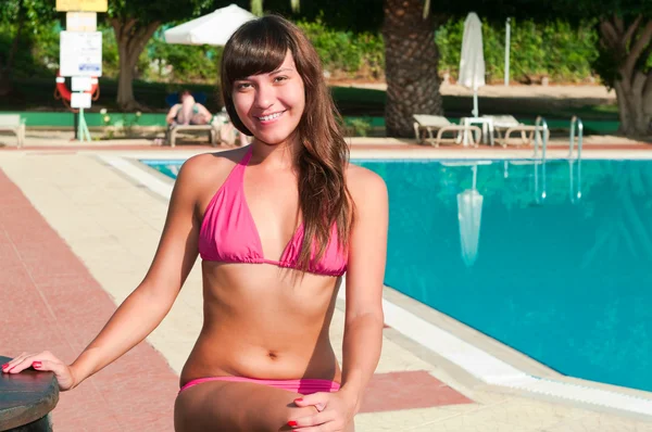 Una chica guapa en bikini sentados alrededor de una piscina con azul — Foto de Stock