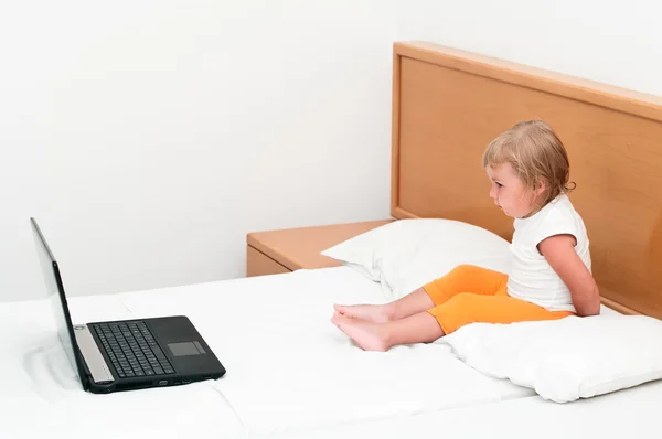 Klein kind zit met een laptop op het bed. — Stockfoto