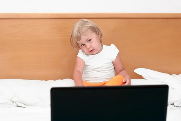 Lilla barnet sitter med en bärbar dator i sängen. — Stockfoto