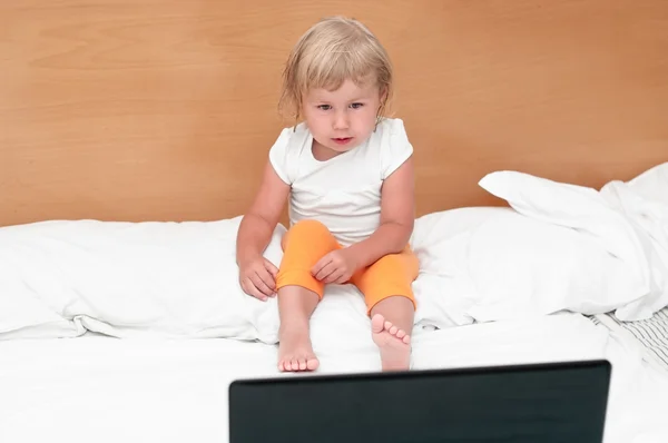 Μικρό παιδί κάθεται με ένα laptop στο κρεβάτι. — Φωτογραφία Αρχείου