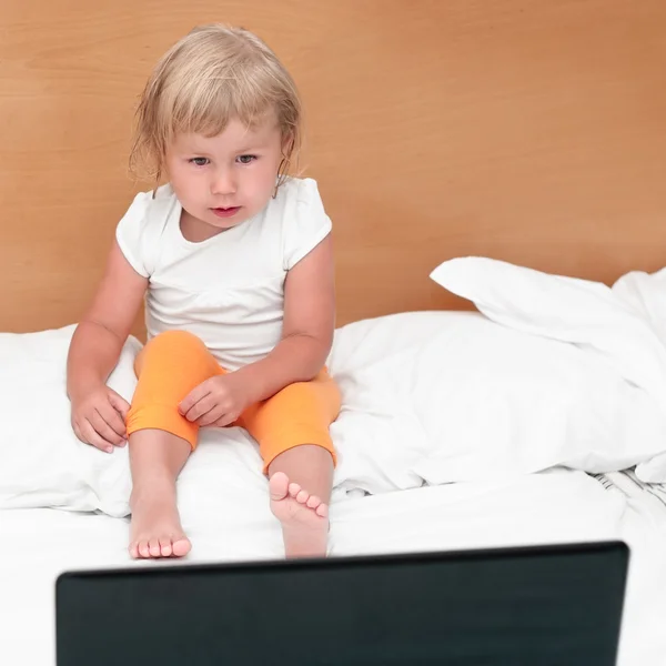 Criança sentada com um laptop na cama . — Fotografia de Stock