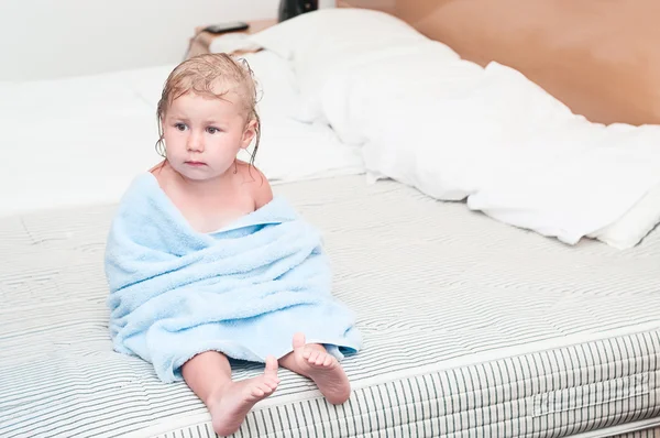 Маленька дитина в рушнику сидить на ліжку — стокове фото