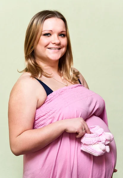 Těhotná mladá žena drží v ruce baby růžové botičky — Stock fotografie