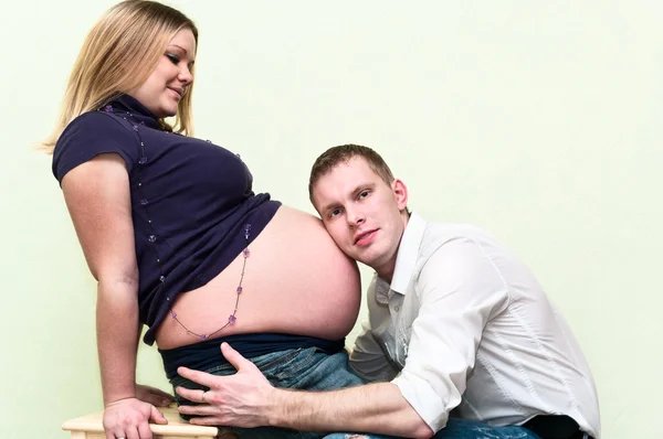 Zwangere vrouw met haar echtgenoot hoorzitting buik. — Stockfoto
