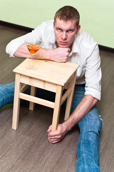 醉酒的男子坐在地板上有酒精的玻璃和持有凳 — 图库照片