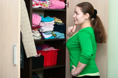 Young woman thinking about to put on near wardrobe clipart