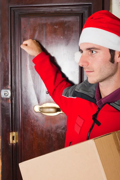 Lieferjunge mit Weihnachtsmütze klopft an die Tür — Stockfoto