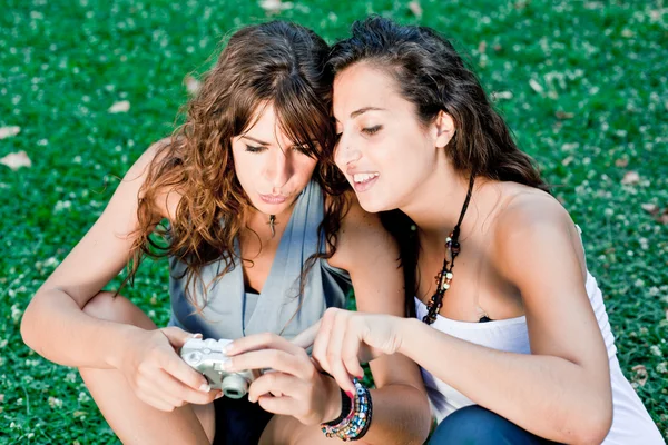 Две девушки в парке смотрят фотографии в камеру — стоковое фото