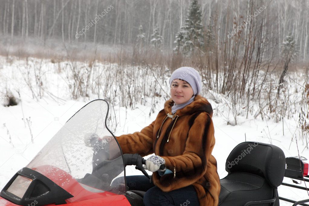 The woman poses on snowmobile in forest