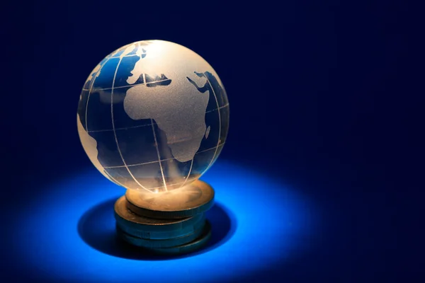 Szkło Globe Leży Stosie Monet Ciemnym Niebieskim Tle Efektu Oświetlenia — Zdjęcie stockowe
