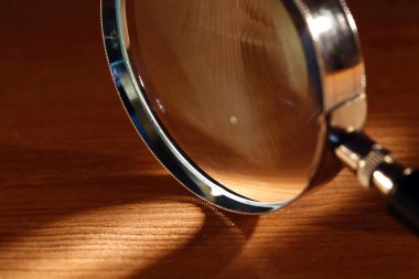 Extreme closeup of magnifying glass standing on wooden surface with beam of light