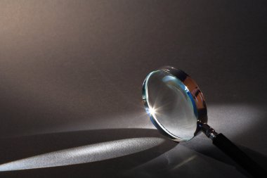 Closeup of magnifying glass standing on dark surface with beam of light clipart