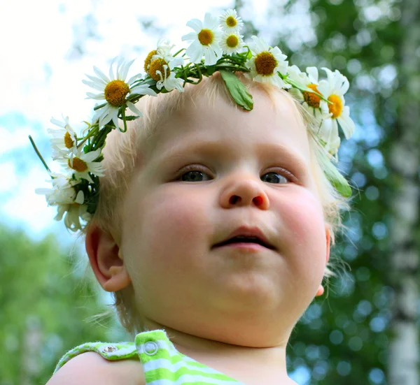 Счастливая маленькая девочка в цветах венок лежит на зеленом лугу — стоковое фото