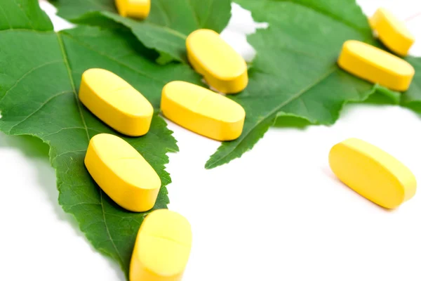 Sarı vitamin hapları üzerinde yeşil yaprakları — Stok fotoğraf