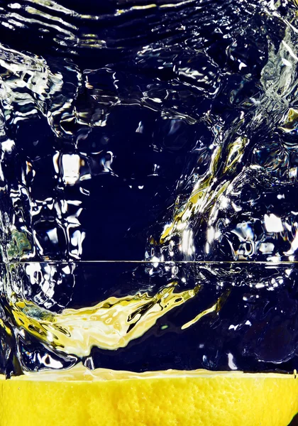 Fél citrom esik le a pohár vízzel a mély kék — Stock Fotó