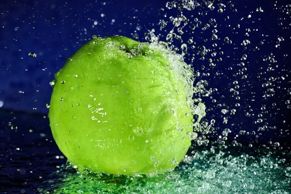 Whole green apple with stopped motion water drops on deep blue — Stock Photo, Image