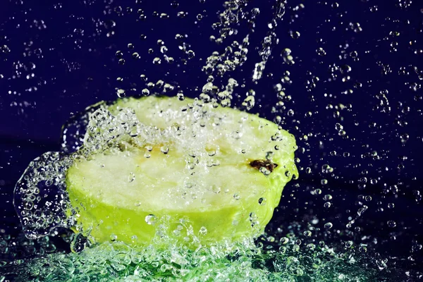 La mitad de la manzana verde con movimiento detenido gotas de agua en azul profundo — Foto de Stock