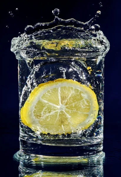 Setengah lemon jatuh ke bawah dalam gelas dengan air di biru tua — Stok Foto