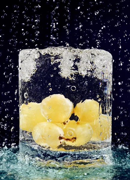 Kiść winogron biały spada w szkle z wody na głębokie b — Zdjęcie stockowe