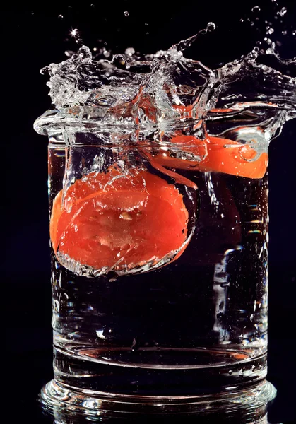 Röd tomat faller ner i glas med vatten på djup blå — Stockfoto