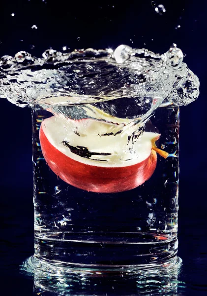 Φέτα κόκκινο μήλο που πέφτει σε ποτήρι με νερό στο απέραντο γαλάζιο — Φωτογραφία Αρχείου