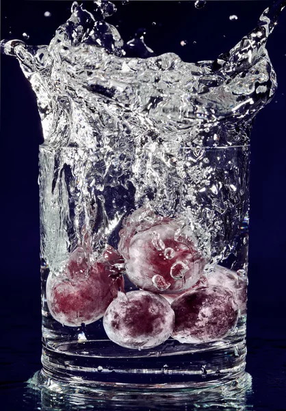 深いブルーのガラスの水で落ちる赤いブドウの房 — ストック写真